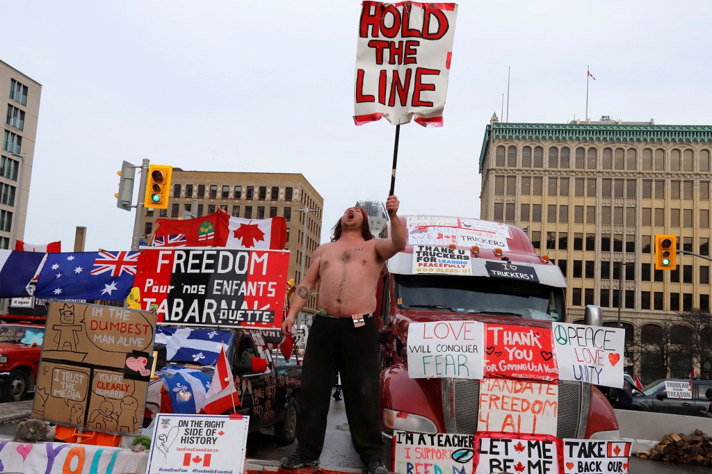 Una persona tiene un cartello davanti ai camion che bloccano una strada del centro mentre i conducenti di camion e i loro sostenitori continuano a protestare contro i mandati per un vaccino contro il coronavirus (COVID-19) a Ottawa, Ontario, Canada.