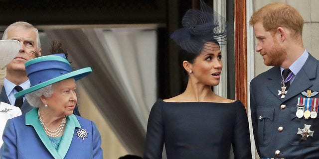 La regina Elisabetta, Meghan Markle e il principe Harry in piedi su un balcone per guardare un volo della RAF su Buckingham Palace nel 2018.
