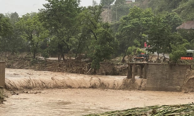 Un'auto si trova accanto a una sezione di un ponte che è stato spazzato via dalle acque alluvionali a Qingyang, nel nord-ovest della Cina